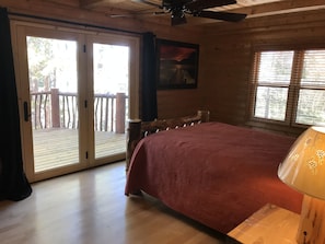 A room with a bed, a wooden headboard, a ceiling fan, a window with blinds, and a door leading to an outdoor deck.