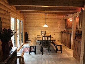A wooden interior with a dining table, chairs, a bench, a hanging light fixture, and a kitchen area with cabinets and a countertop.