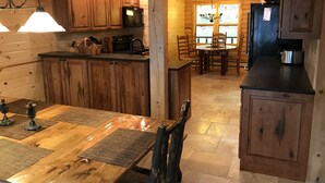 Interior de una cabaña de madera con cocina, comedor y un ventanal grande.