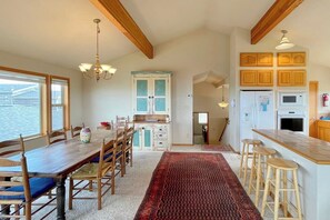 A spacious kitchen with wooden cabinets, a dining area with a long table and chairs, and a view through the window.