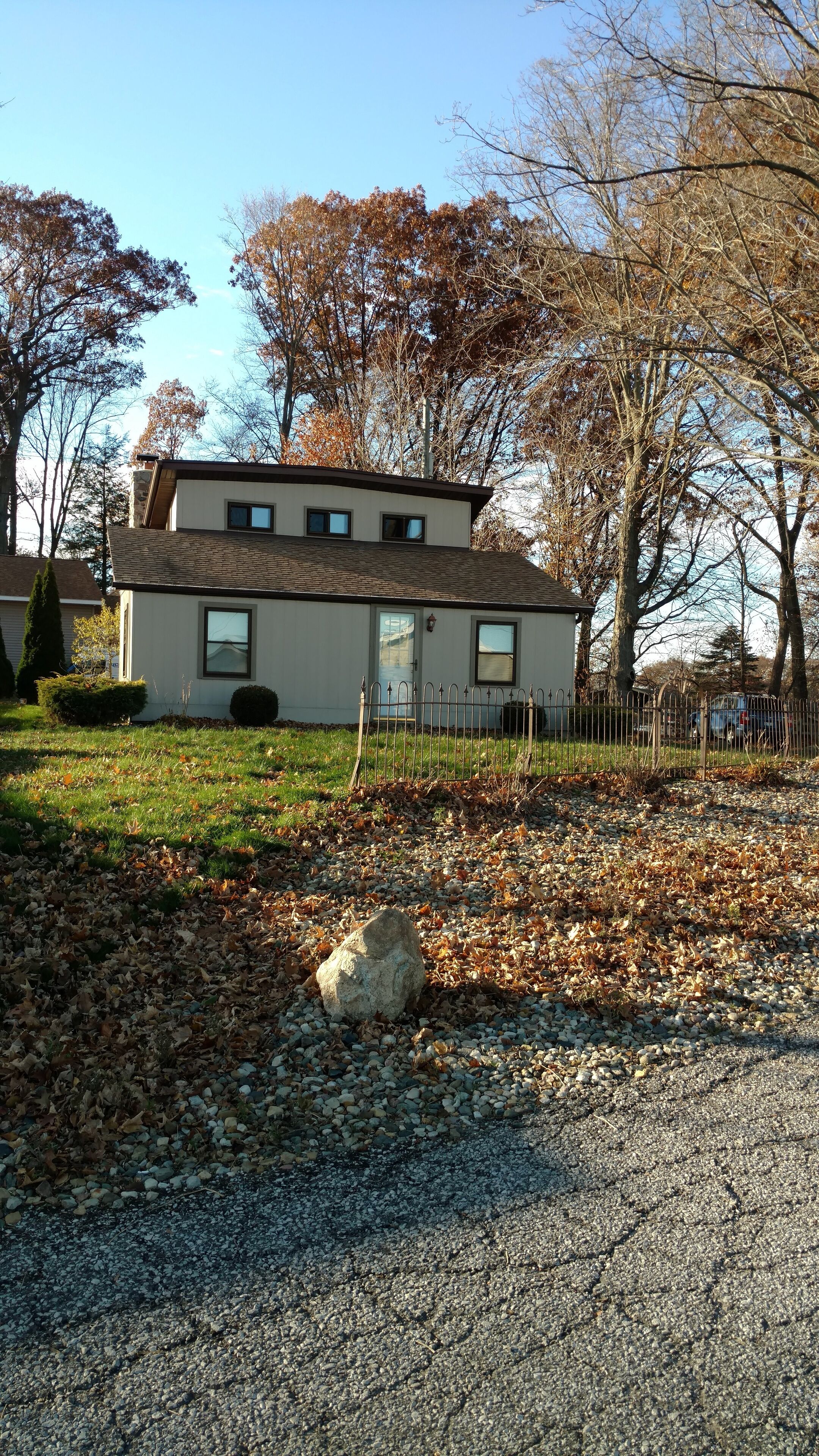 Une maison à deux étages avec un toit en pente, un porche à l’avant et une allée gravillonnée.