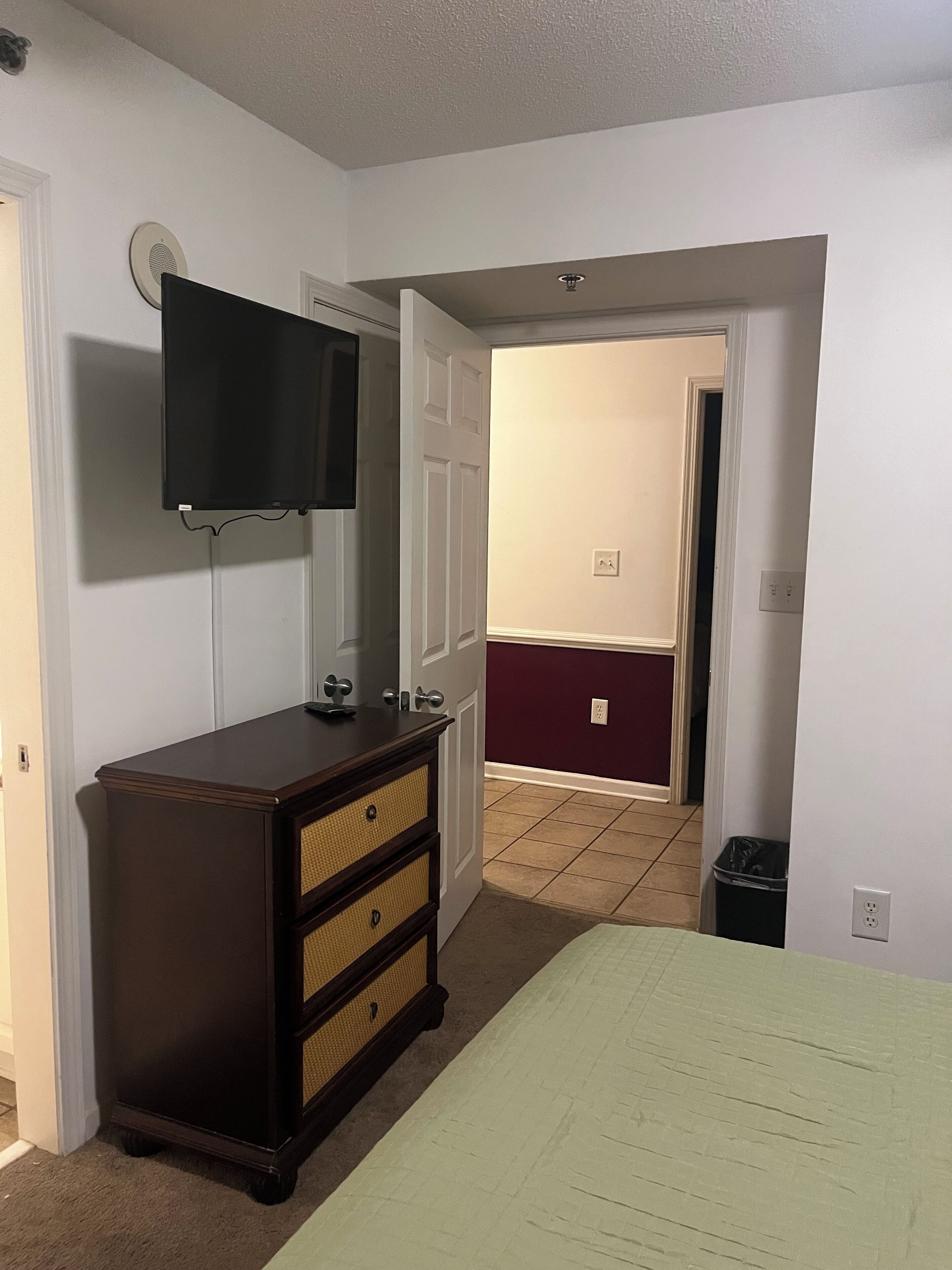 A bedroom with a bed, dresser, television, and a door leading to another room.