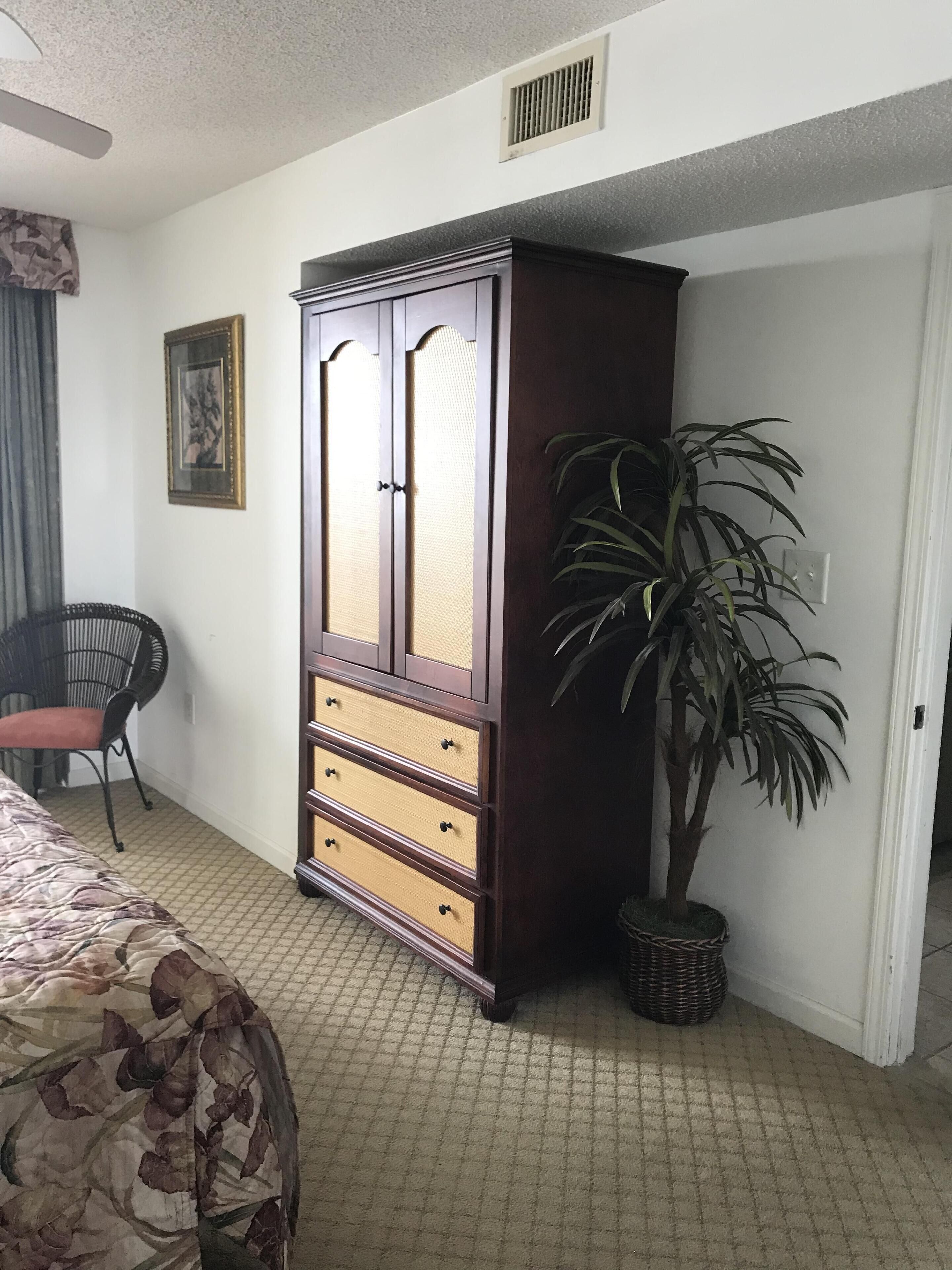 A bedroom with a bed, a wardrobe, a chair, and a potted plant.
