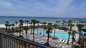 A pool area with lounge chairs and palm trees, overlooking a beach and ocean. - Dunes of Panama C302 — Sept 1-12 SPECIAL — with Deluxe Free BEACH CHAIR Rentals (Panama City)
