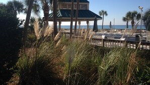 A beachside restaurant with outdoor seating, palm trees, and a view of the ocean. - Dunes of Panama C302 — Sept 1-12 SPECIAL — with Deluxe Free BEACH CHAIR Rentals (Panama City)