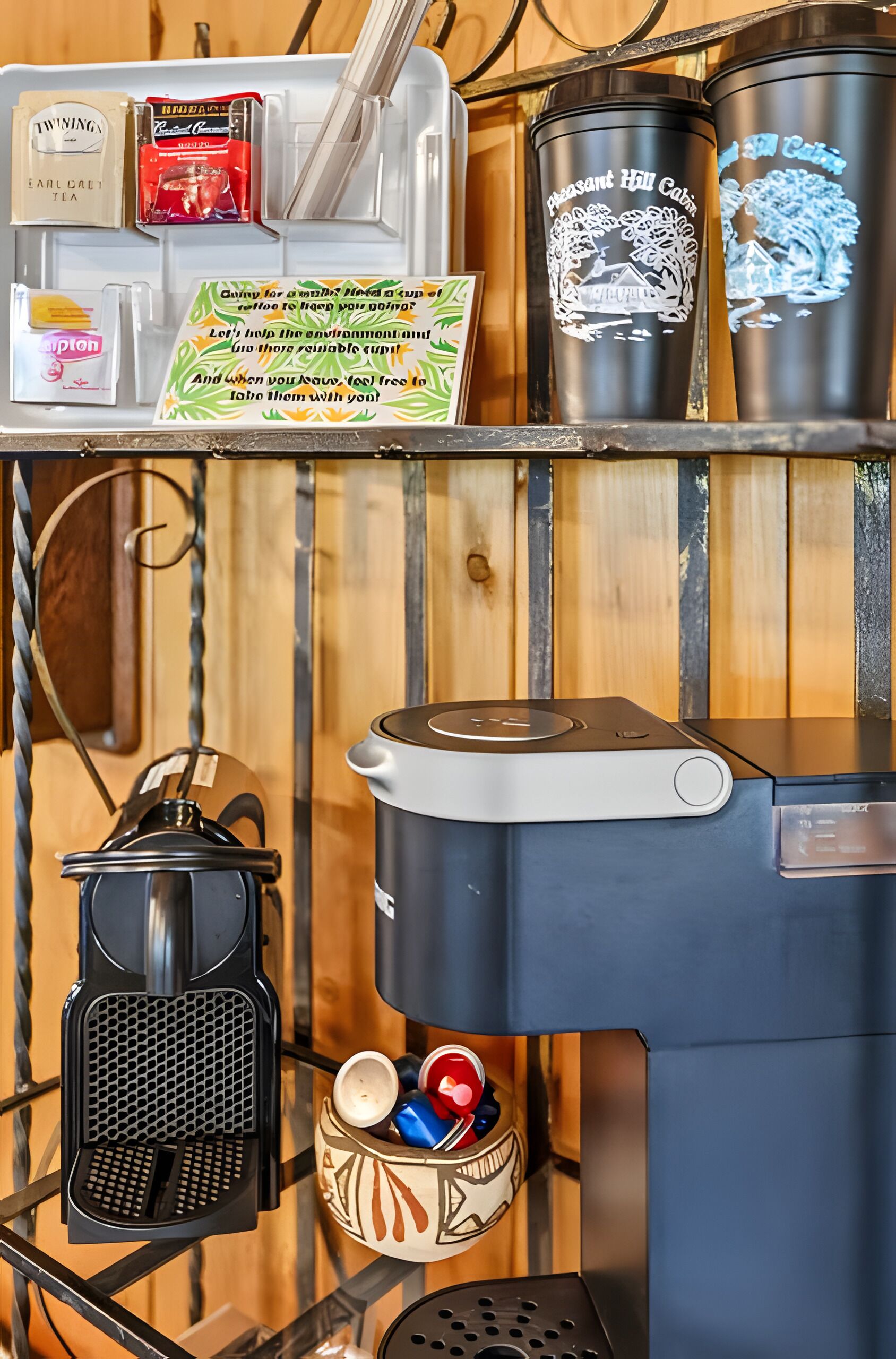 Une machine à café avec un panier rempli de tasses et un panneau encourageant l’utilisation de tasses réutilisables.
