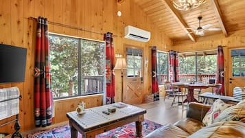 A cozy cabin interior with wooden walls, large windows, a dining area, and a fireplace.