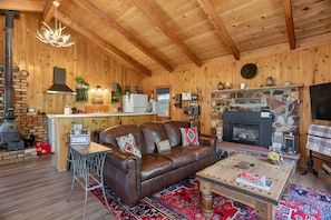 L’intérieur chaleureux d’un chalet avec un plafond en bois, une cheminée, un canapé en cuir et une table à manger.