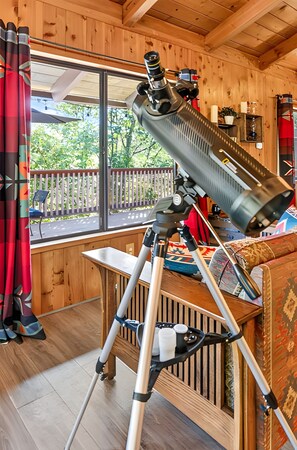 Een telescoop op een statief in een houten kamer met een raam dat uitkijkt over een terras.