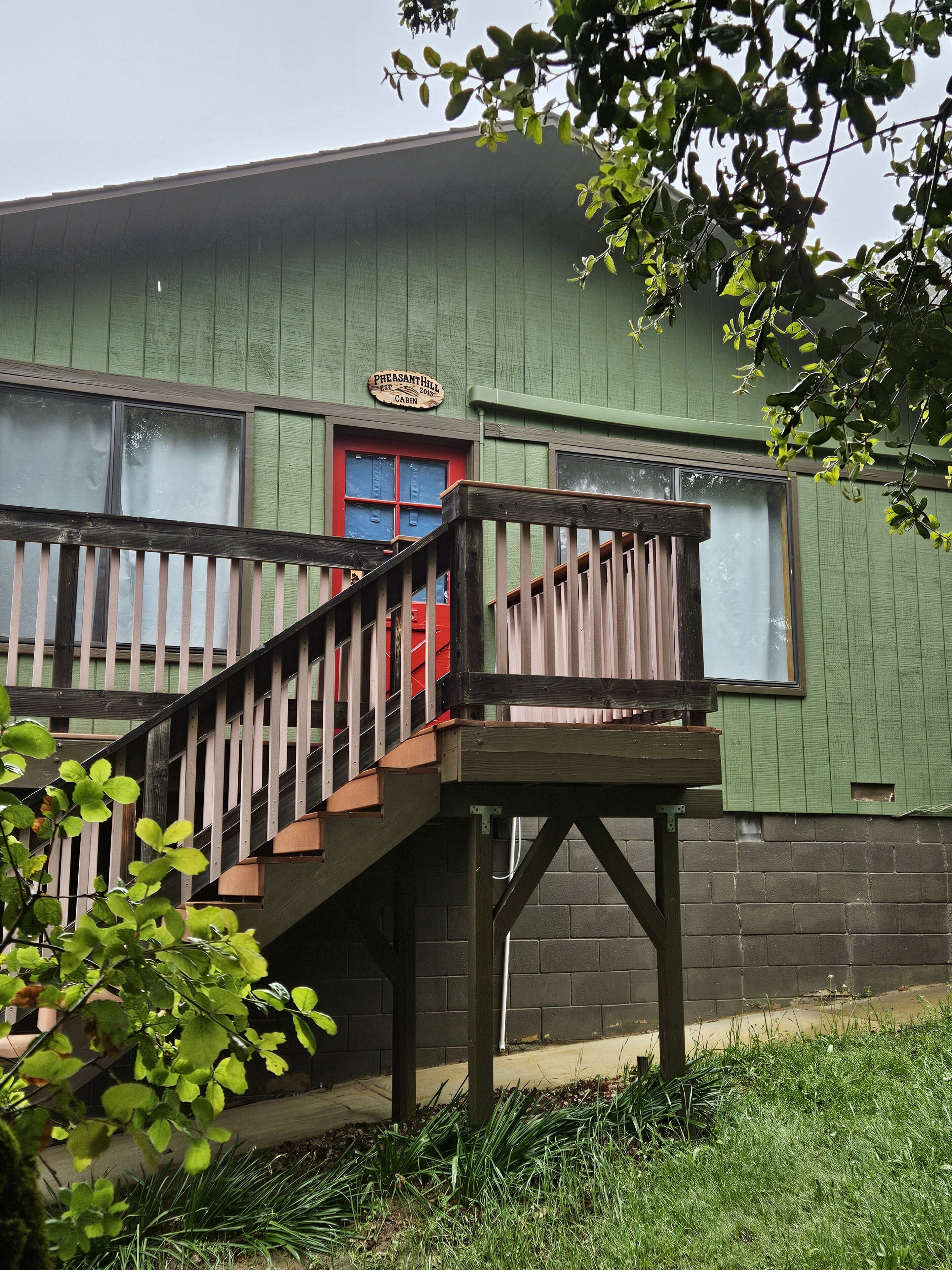 A green building with a red door and a wooden staircase leading to a balcony.