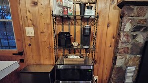 A compact kitchen with a microwave, coffee maker, and a shelf with various items.