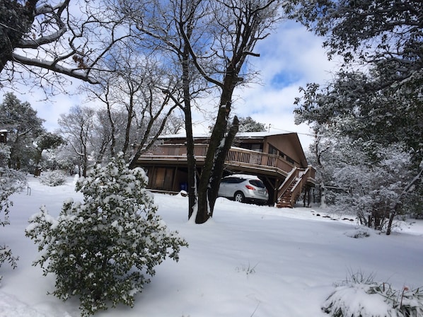 Una cabaña de madera con balcón y una escalera que lleva a una terraza, rodeada de árboles cubiertos de nieve.