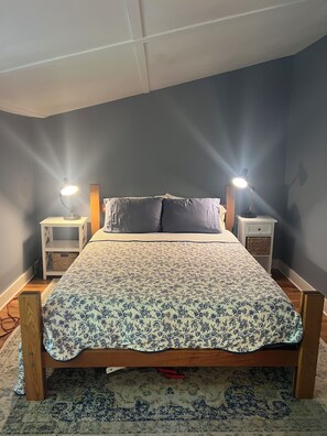 Una camera da letto con un letto, due comodini con lampade, una coperta a motivi decorativi e una testiera in legno.