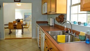 A kitchen with wooden cabinets, a stainless steel sink, and a dining area with a table and chairs. - Spacious, light-filled mid-century home in Old Town (Bay Saint Louis)