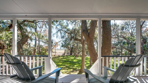 Un portico coperto con due poltrone Adirondack rivolte verso una zona erbosa con alberi.