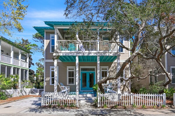 A two-story building with a balcony, a blue door, and a white picket fence.