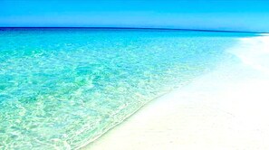 En strand med kristallklart, turkosfärgat vatten och vit sand.