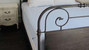 A bed with a metal frame, white bedding, and two wall-mounted light fixtures. - Historic 1887 Carriage House Located On Landmark Property (Santa Cruz)