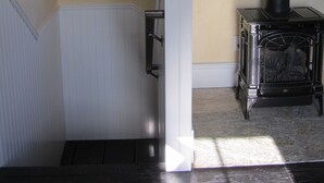 A room with a white staircase, a window with a view of trees, and a black wood-burning stove. - Historic 1887 Carriage House Located On Landmark Property (Santa Cruz)