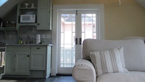 A kitchen with white cabinets, a microwave, and a window. There is a beige couch with a striped pillow. - Historic 1887 Carriage House Located On Landmark Property (Santa Cruz)