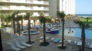 Un área de piscina en un complejo turístico, con varias piscinas, sillas de descanso y palmeras.