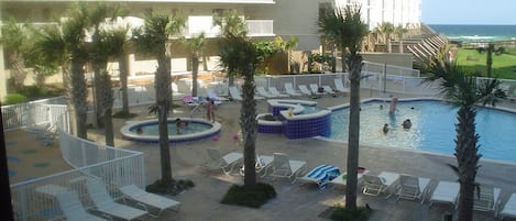 Área de piscina de resort com várias piscinas, espreguiçadeiras e palmeiras.