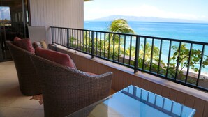 Un balcone con mobili in vimini, un tavolo di vetro e vista sull'oceano e sulla spiaggia.