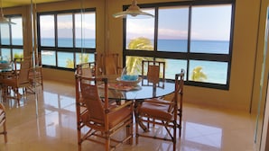 Un'area pranzo con tavolo e sedie in vetro, ampie finestre vista mare e una lampada a soffitto.