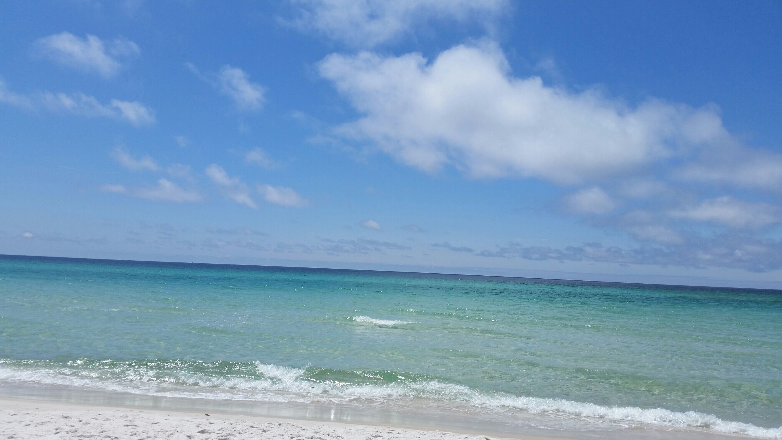 A beach with clear turquoise water and a sandy shore under a partly cloudy sky.