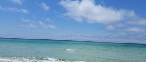 A beach with clear turquoise water and a sandy shore under a partly cloudy sky.