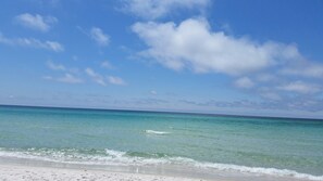 En strand med klart turkis vand og en sandet kystlinje under en delvist overskyet himmel.