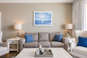 Ein modernes Wohnzimmer mit einem beigefarbenen Sofa, zwei Nachttischen mit Lampen, einem Couchtisch mit Dekoration und einem gerahmten Gemälde an der Wand.