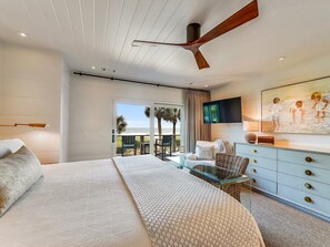 Un dormitorio con cama, escritorio, televisor y balcón con vista al océano.
