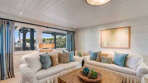 Una sala moderna con un sofá blanco, una mesa de centro de madera y un ventanal con cortinas.