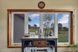 Una encimera de cocina con un cartel de bar sobre un ventanal grande, un fregadero y diversos utensilios de cocina.