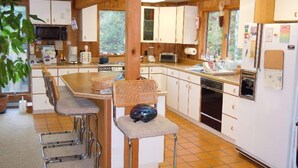 A compact kitchen with white cabinets, a built-in oven, a microwave, and a refrigerator. There are three metal bar stools and a woven chair. - 1-2 Family Perfection:  Location + Views + Ammenities = Value (West Dover)