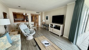 Un salon comprenant un canapé, une table basse, un meuble pour la télévision et donnant sur la cuisine et l’espace repas.