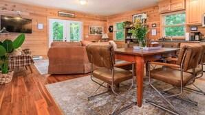 Interior acolhedor de cabana, com decoração em madeira, área de jantar com mesa e cadeiras, e cozinha com pia e armários.