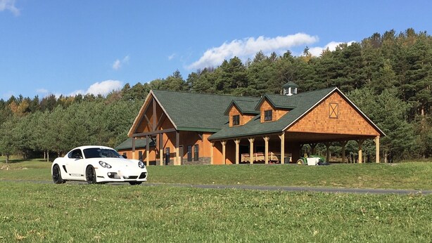 A large wooden cabin with a green roof, surrounded by a grassy field and forested hills. - Finger lakes region outdoor getaway (Lafayette)