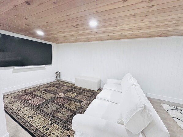 A room with a white sofa, a patterned rug, and a flat-screen TV mounted on the wall.