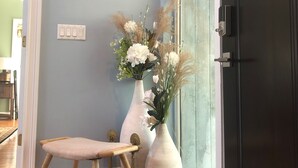 A room with a wooden bench, a white vase with flowers, a light switch, and a coat rack.