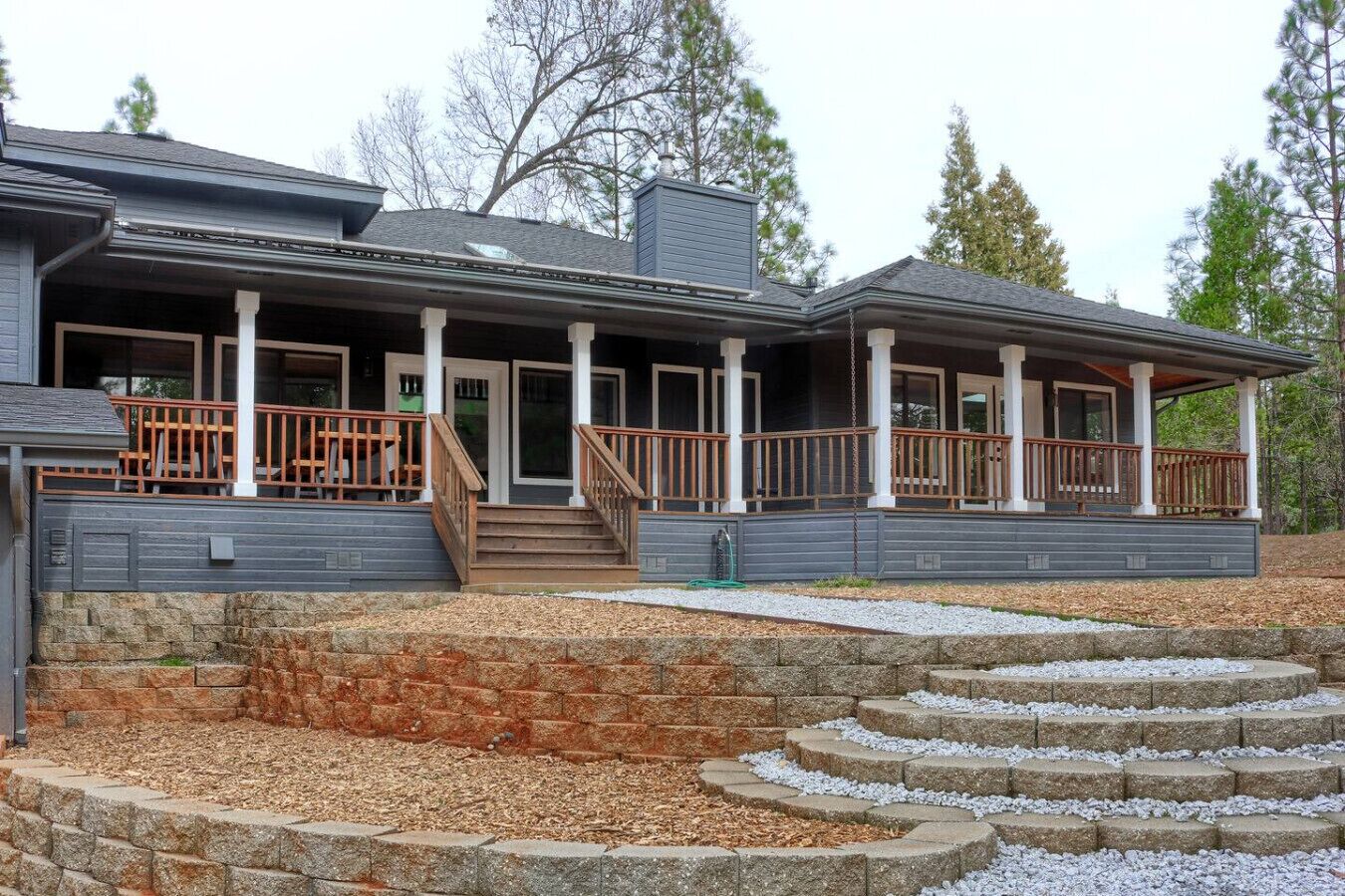 A two-story house with a covered porch, stone retaining wall, and a stone staircase leading to the entrance.
