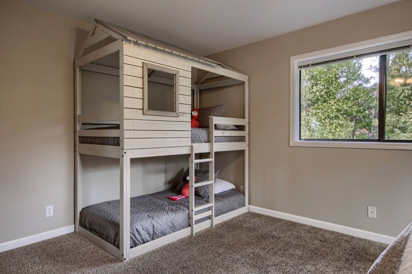 A bunk bed room with a window, carpeted floor, and a small mirror on the upper bunk.