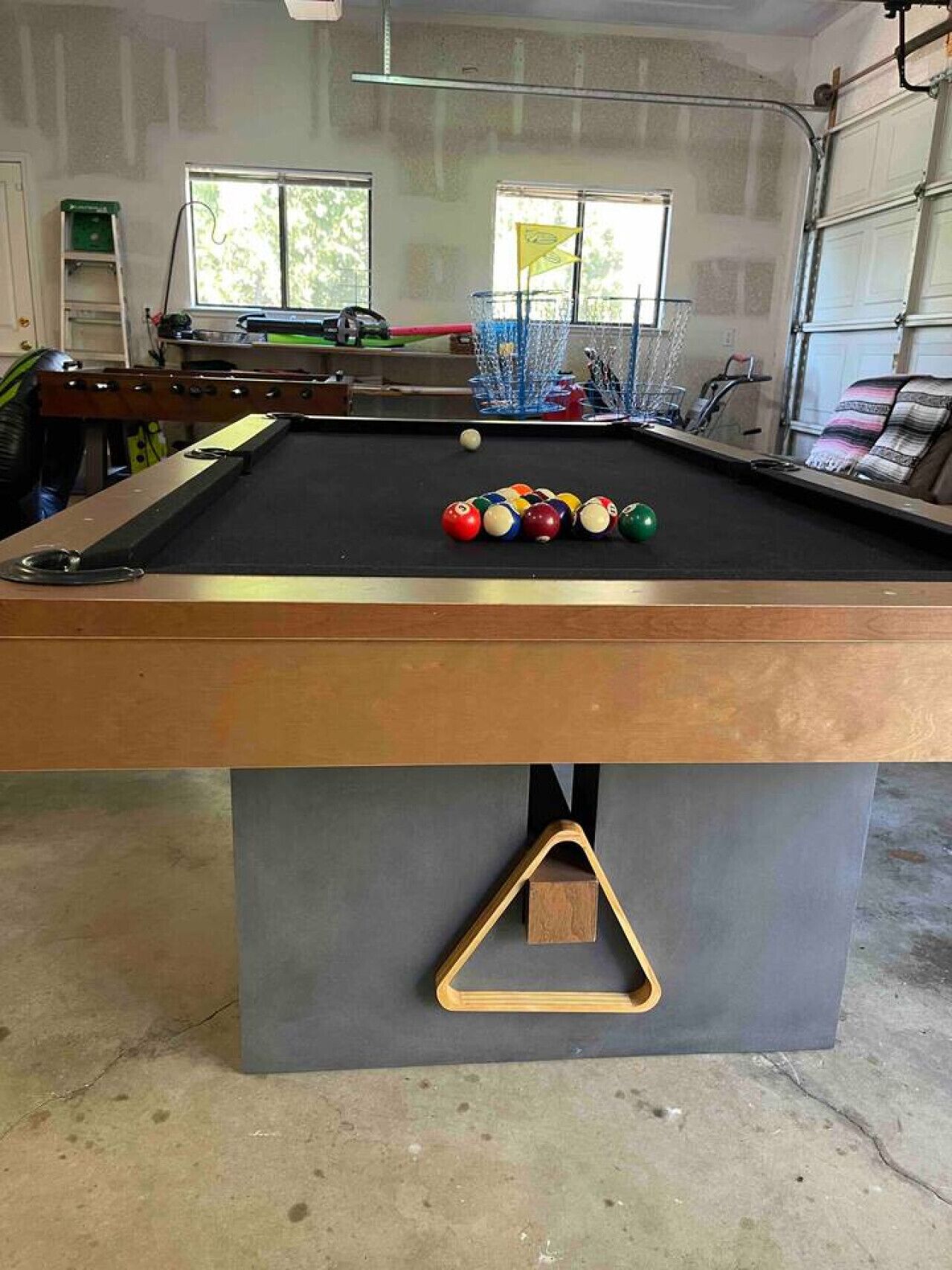 A pool table with balls, a ladder, and a garage door in the background.