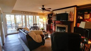 A cozy living room with a sofa, a fireplace, a television, and a sign that reads "LAKE HOUSE".