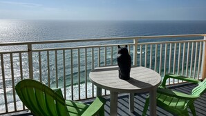 Un balcone con vista sull'oceano, un tavolo e due sedie verdi.