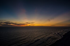 A sunset over a beach with waves and a distant landmass. - Splash resort - Family-friendly - Excellent view - Optional beach services (Panama City Beach)