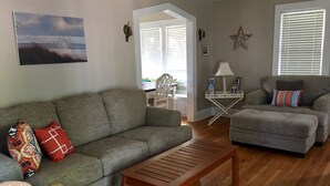 Una sala de estar con un sofá gris, una mesa de centro de madera y un sillón gris. Hay una decoración con forma de estrella en la pared y una lámpara sobre una mesita.