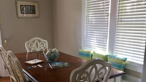 Un comedor con una mesa de madera, sillas blancas y una ventana con persianas.