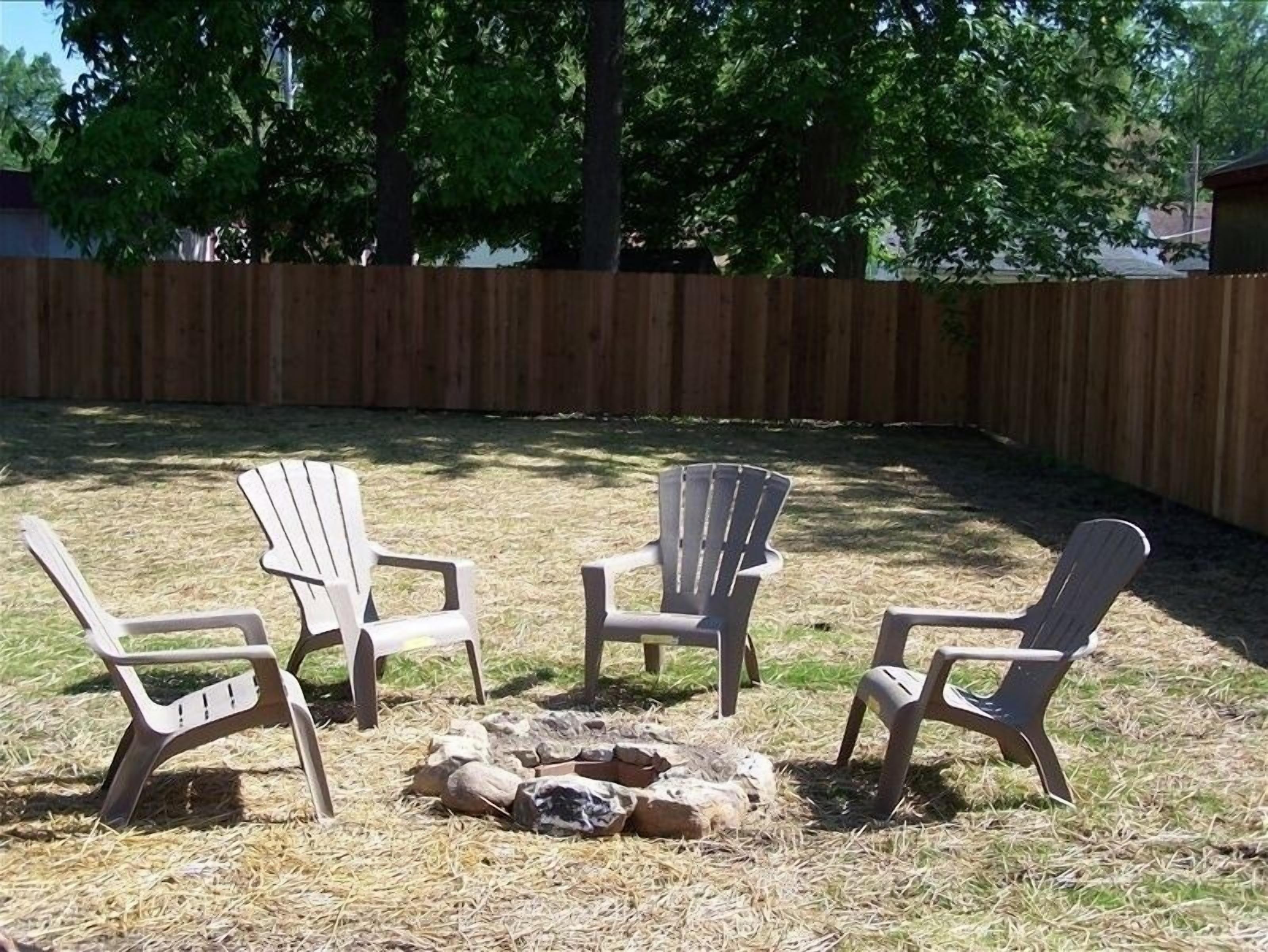 A backyard with four Adirondack chairs arranged around a small fire pit.
